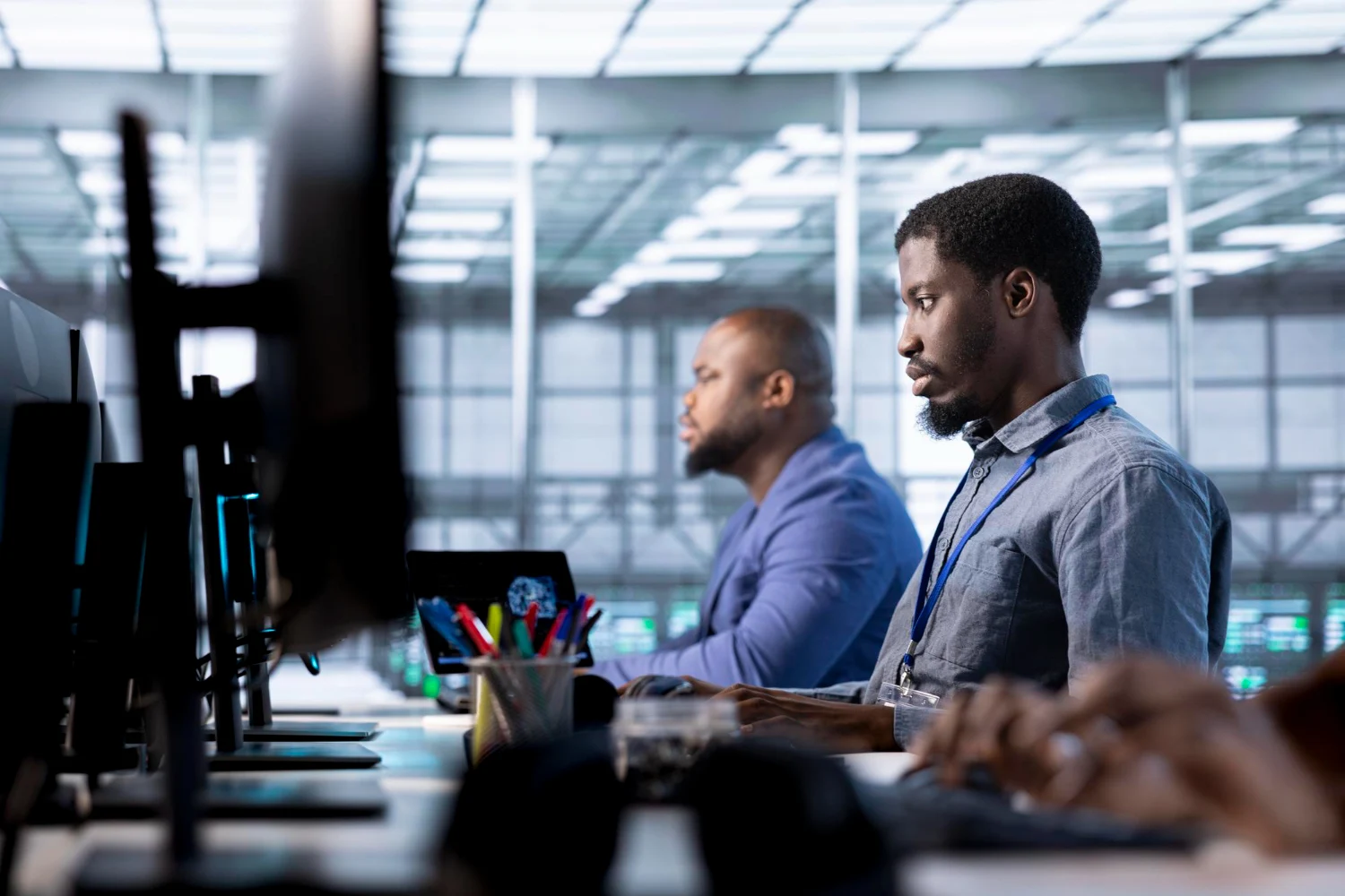 Profissionais trabalhando em um escritório de tecnologia com computadores e ambiente corporativo moderno.