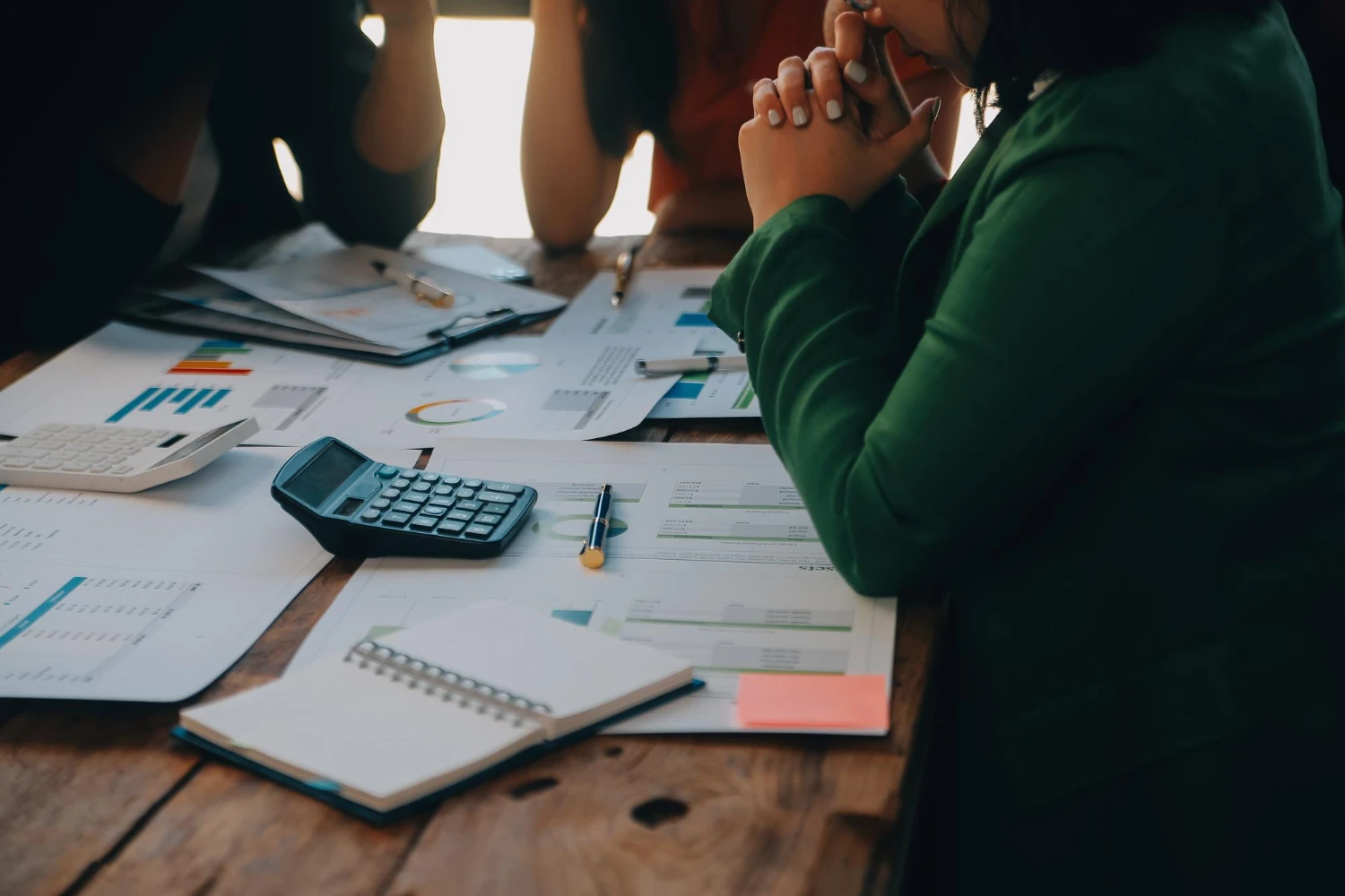 Reunião de análise financeira empresarial Pessoa em reunião de negócios analisando relatórios financeiros sobre uma mesa com calculadora, notebook e gráficos impressos.
