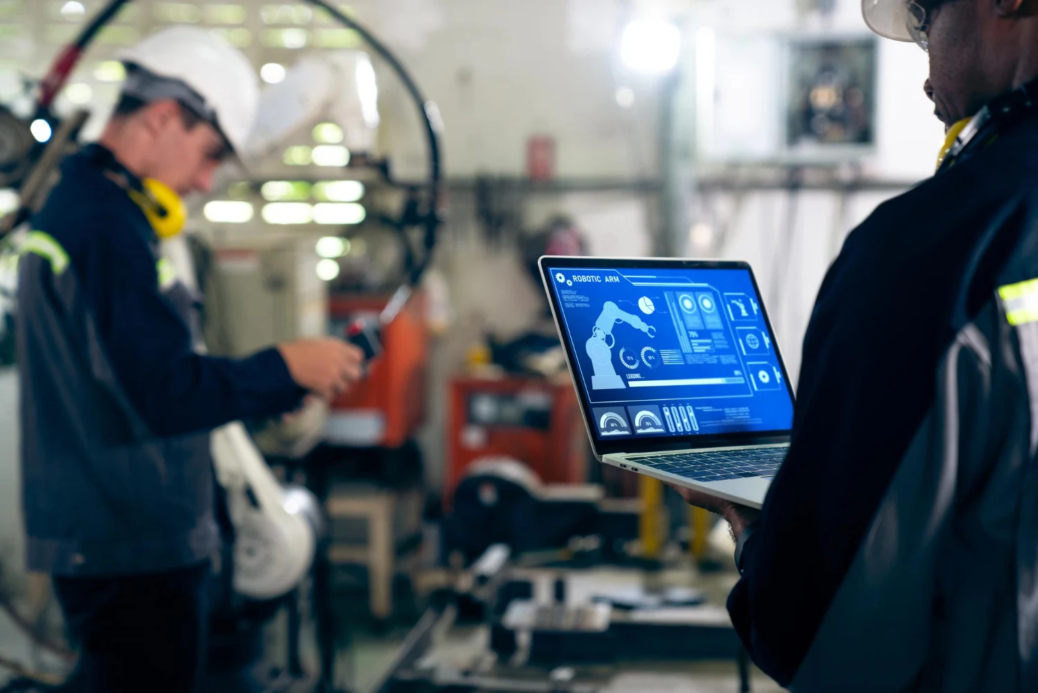 Monitoramento de robô industrial em fábrica automatizada Profissional monitora braço robótico industrial em notebook dentro de uma fábrica automatizada.